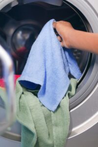 Close-up of a hand placing colorful towels into a front-loading washing machine.