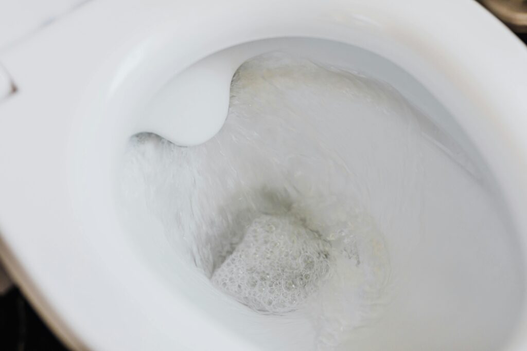 High angle of clean white ceramic toilet bowl with flushing foamy water in bathroom
