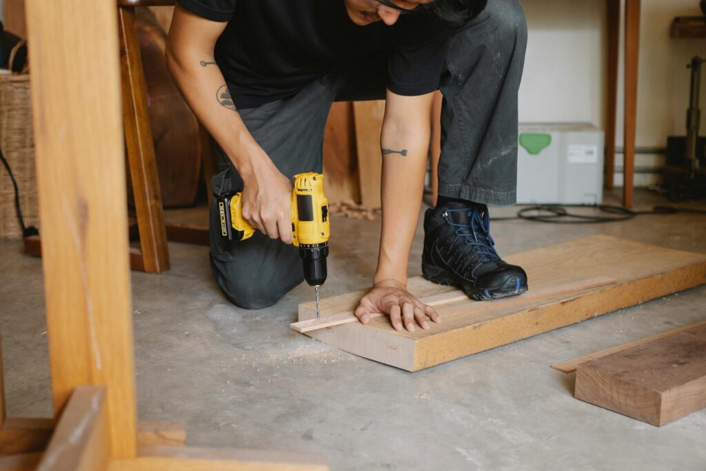 Crop anonymous male drilling piece of timber detail with screwdriver among lumber in workshop